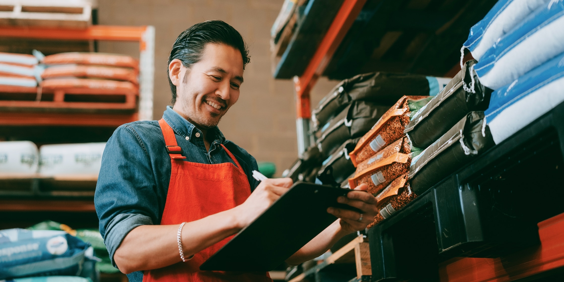 A worker at a hardware store smiles as he writes on his clipboard.