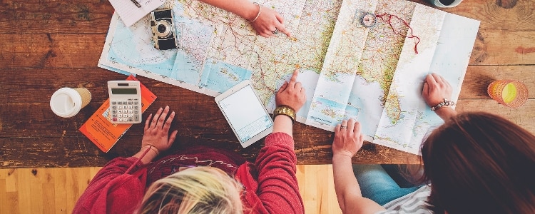 A group of people use a map, calculator and mobile tablet to set a budget and itinerary for their next trip.