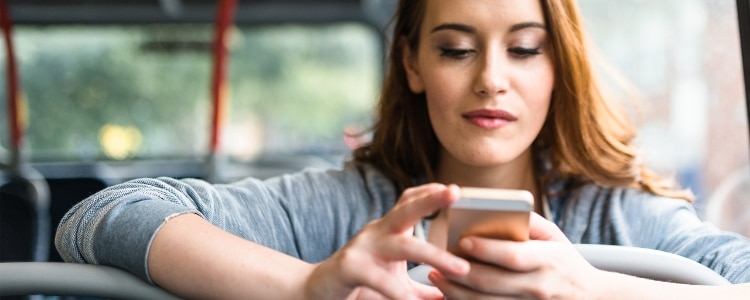 Young woman uses her phone to assess her credit while riding the bus.