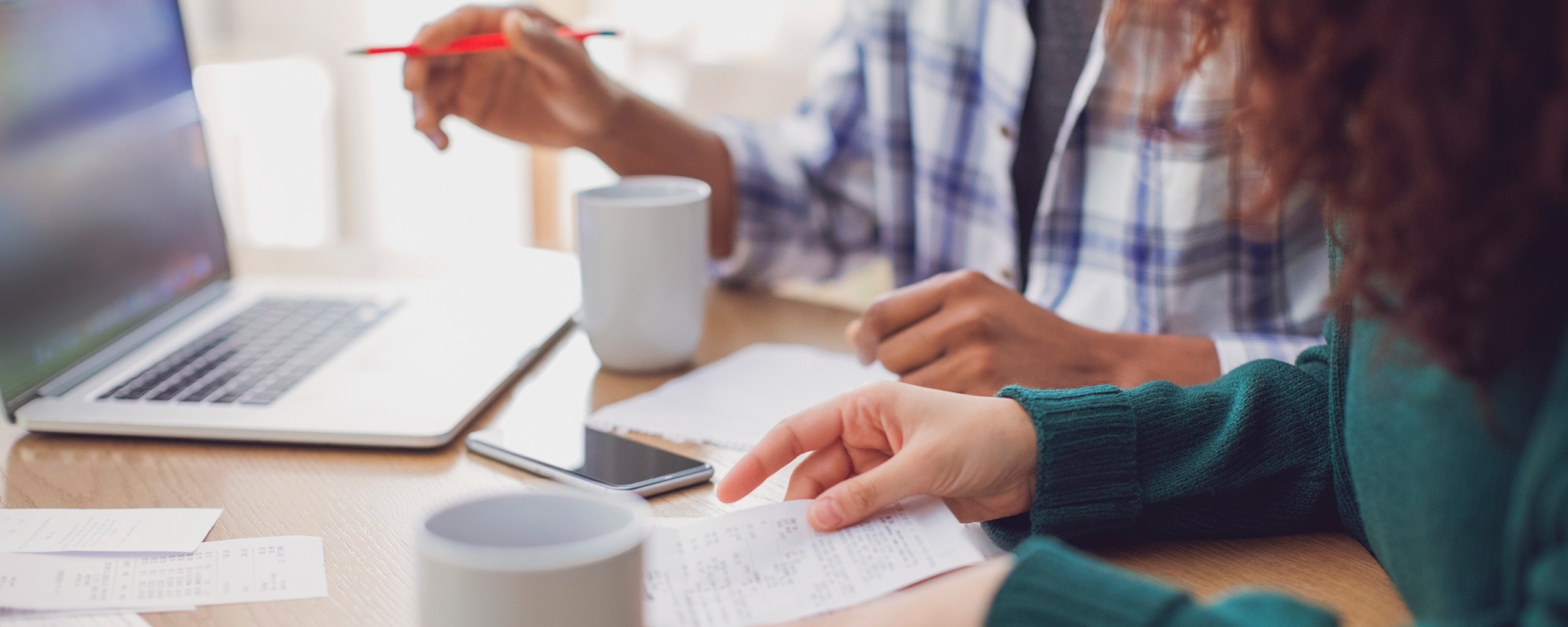 Two people sitting at a table with a computer and paper figuring out their finances.