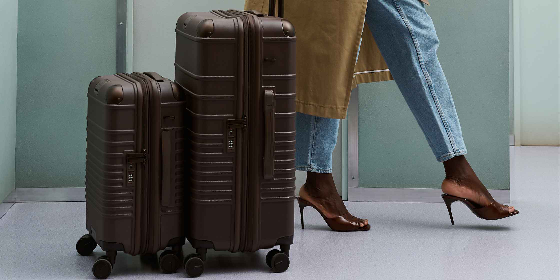 A person in jeans and a long coat pulls rolling suitcases from modern luggage brand BÉIS.
