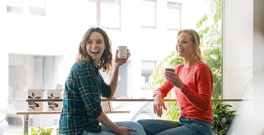 Two people drinking from mugs at a cafe.