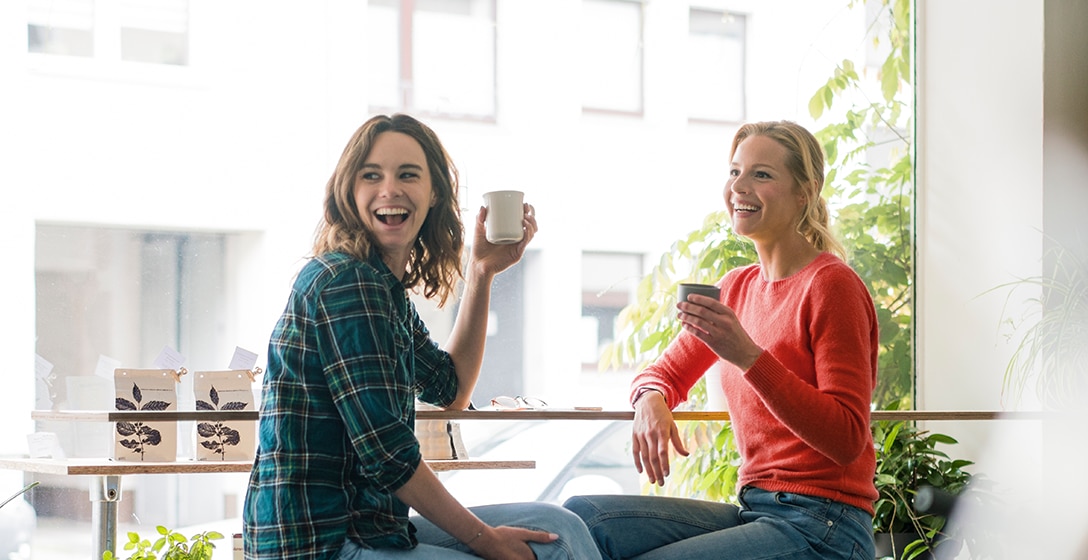Two people drinking from mugs at a cafe.