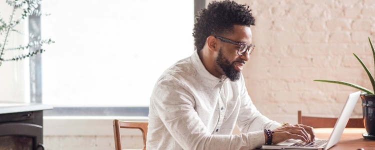 A person in glasses typing on their laptop.