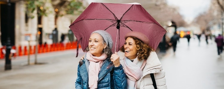 Two smiling people walking under an umbrella on a rainy day.