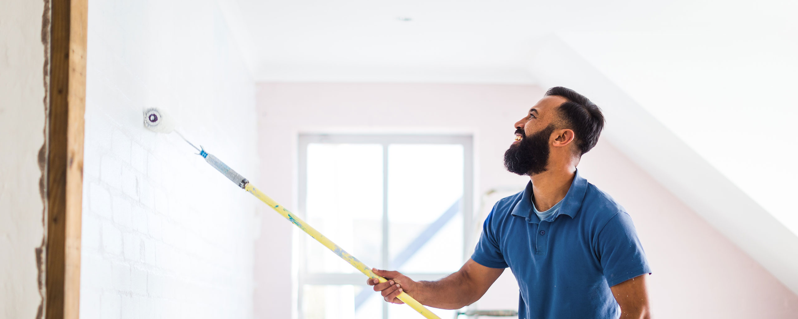 A man uses a paint roller to renovate a room in his house.