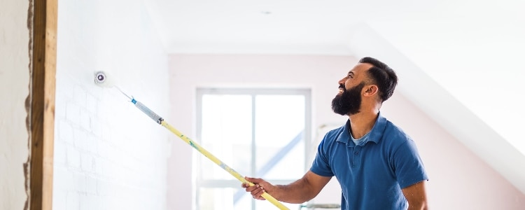 A man uses a paint roller to renovate a room in his house.