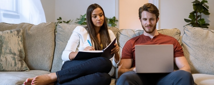 Two people sitting on a couch look at a laptop to see if they should refinance their mortgage.
