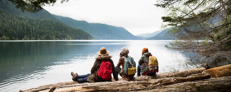 A photo of 3 friends sitting on the bank of a river surrounded by mountains.