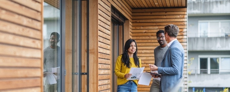 A realtor talks to a couple outside of a home about HOA fees.