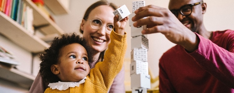 Young couple watch as their toddler plays with a tower of building blocks.