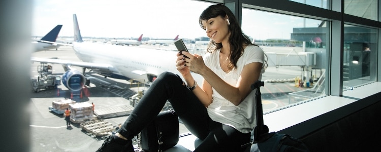 A photo of a person in an airport, reading their phone while waiting to board a fight.