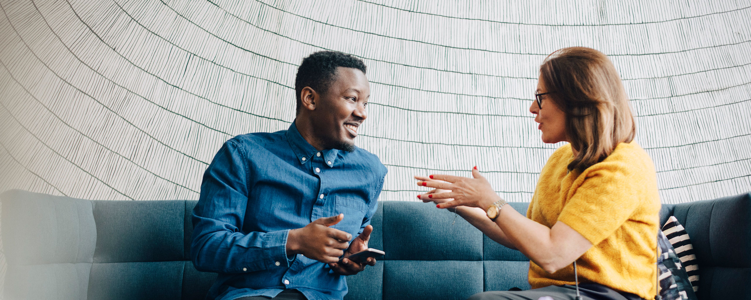 Two people sit on a couch and talk about advice for a job search.