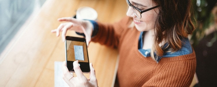 A photo of a person in a coffee shop using their phone to deposit a check into their bank account.