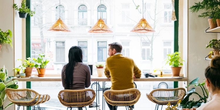 Two people sit in wicker chairs facing a big window.