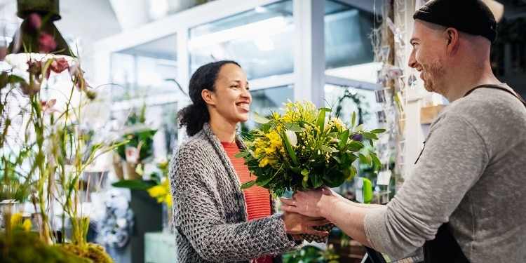 Flower shop vendor hands a bouquet to a customer.
