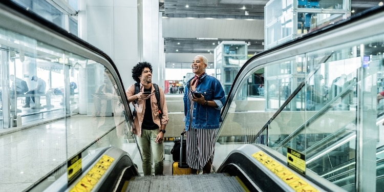 Smiling travelers ascending the escalator at the airport.