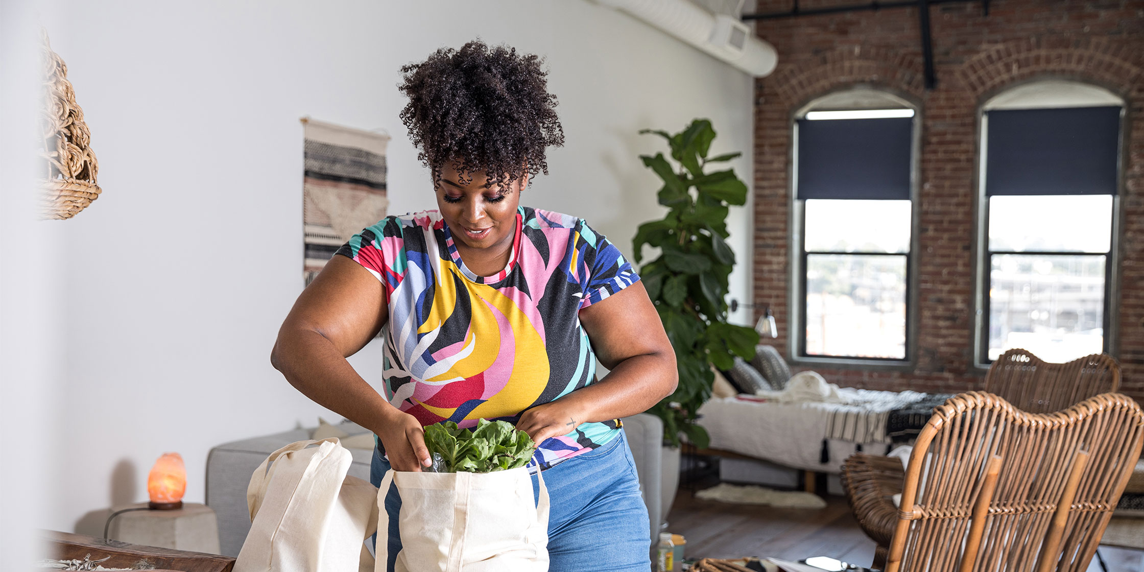 A person in a home lifts leafy greens out of a canvas tote bag.