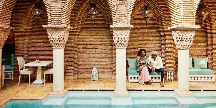 A smiling couple sitting outside by the pool while on vacation.