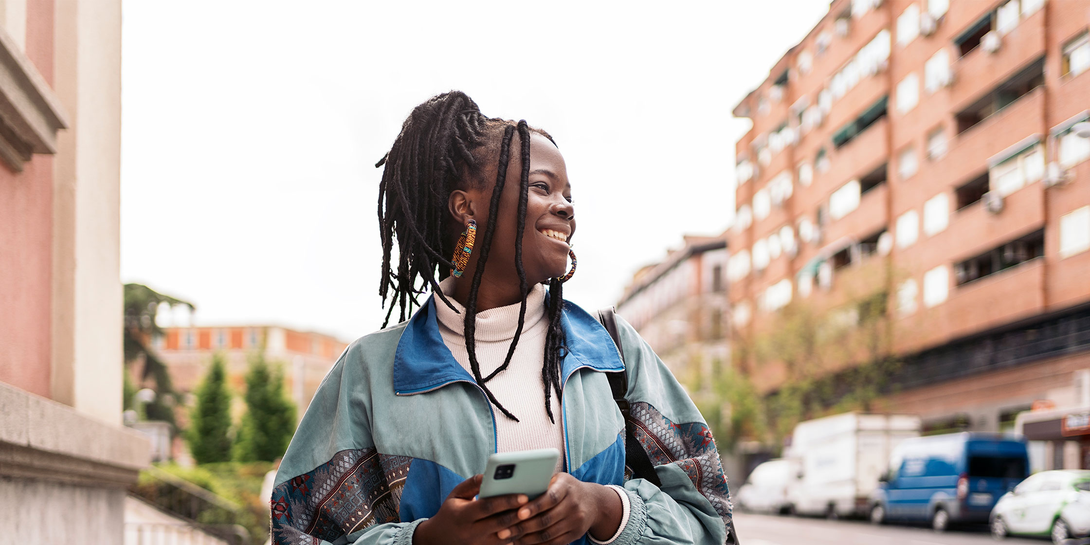 A person stands outside smiling while holding a cellphone.