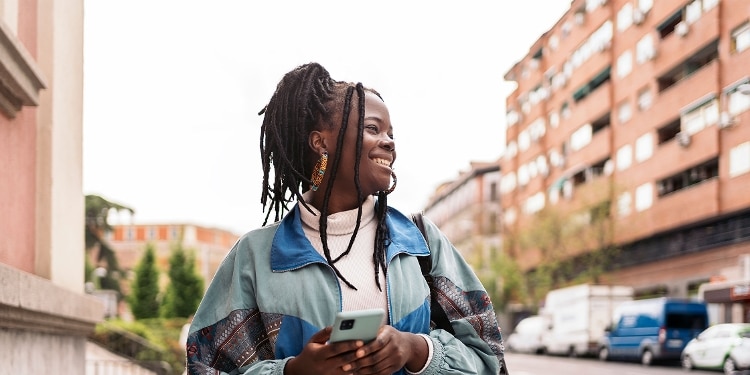 A person stands outside smiling while holding a cellphone.