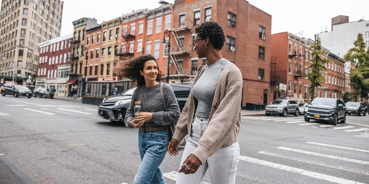 Two people talk as they cross a busy city road.