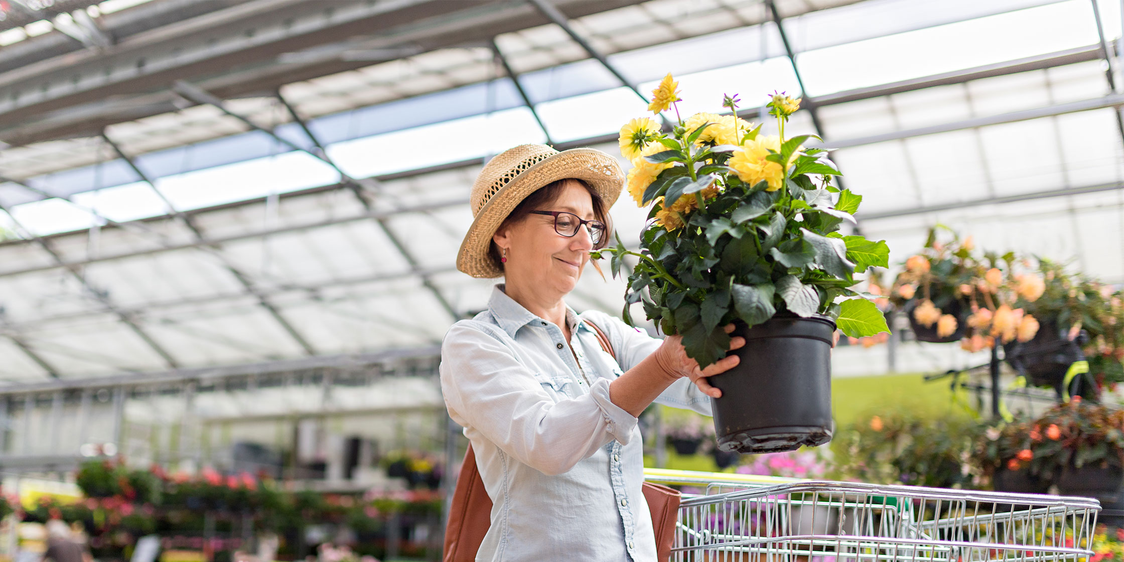 A woman puts a plant into her shopping cart at a garden center.