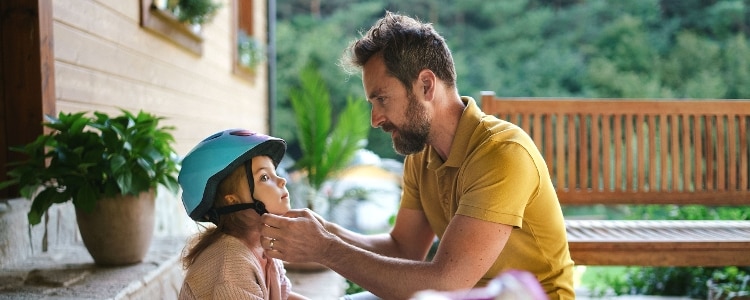 A father helps his daughter put on a bicycle helmet.