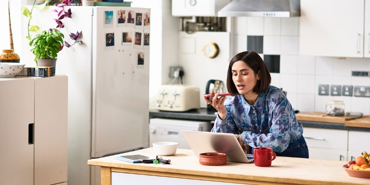 A person in a kitchen talks on the phone while using a laptop to freeze her Experian credit report