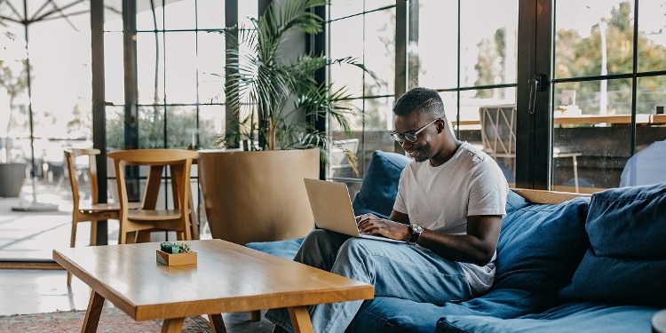 A photo of a person sitting on a couch, using their laptop to learn more about budgeting with credit cards.