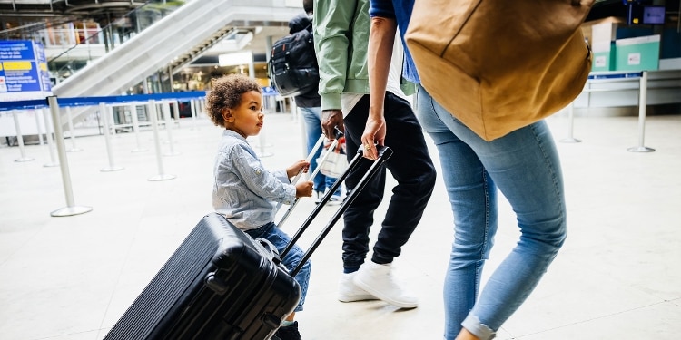 Two adults walking through an airport pulling rolling suitcases, with a young child riding on one.