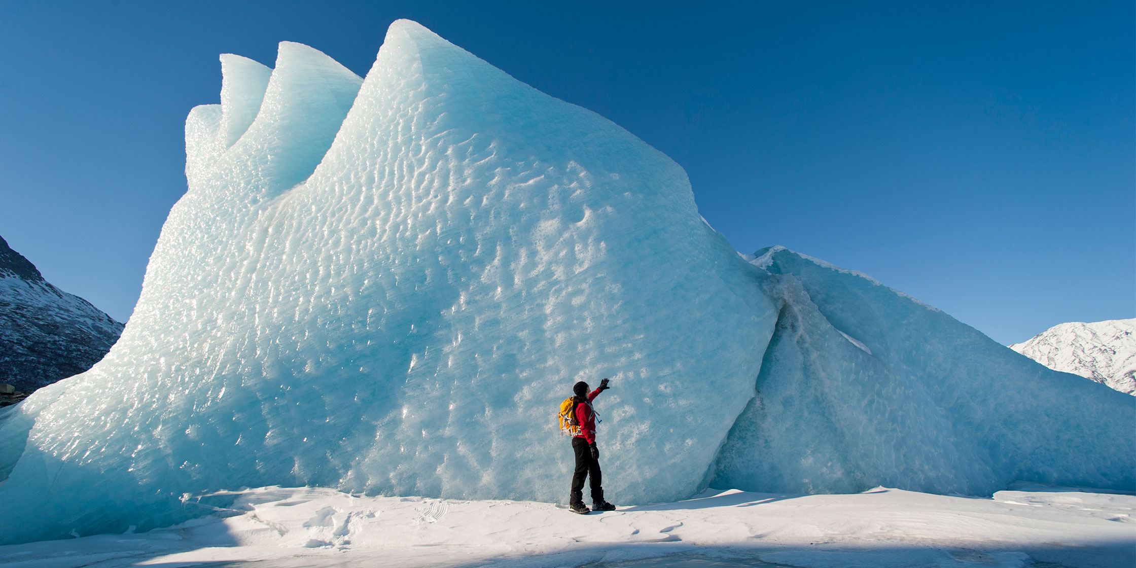 A hiker stands in front of an ice formation on the Knik Glacier in Alaska.