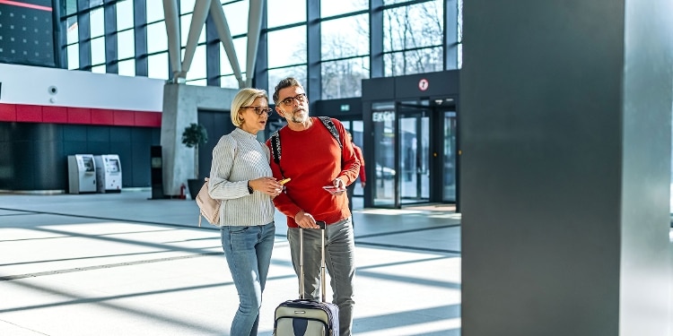 A photo of two people at the airport, one with a rolling suitcase.