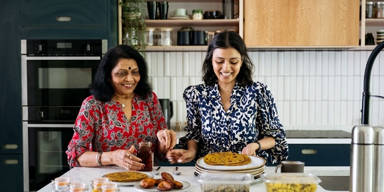 Two people stand side by side at a kitchen counter. The younger one puts crispy flatbread on plates.