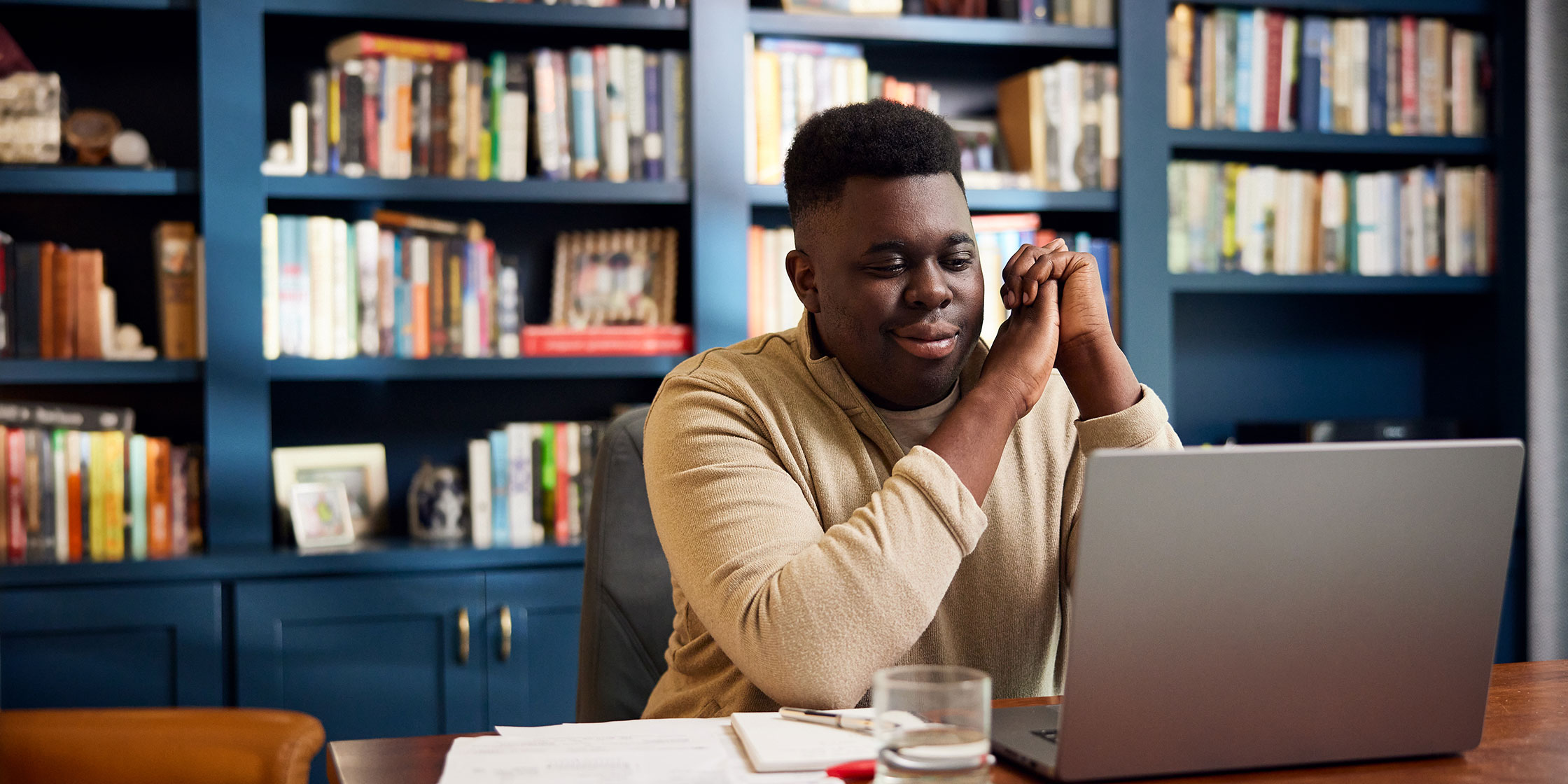 A person sitting at a table in front of a bookshelf while using their laptop.