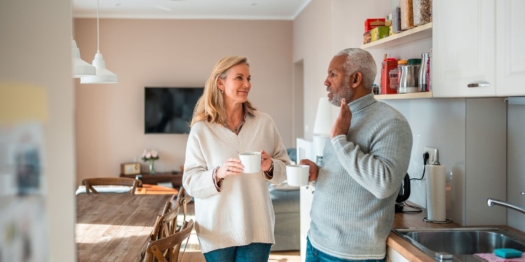 Two people stand in a well-lit kitchen drinking coffee and talking.