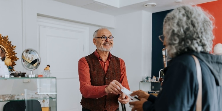 A smiling person in glasses hands a prepaid card back to someone who has just made a purchase.