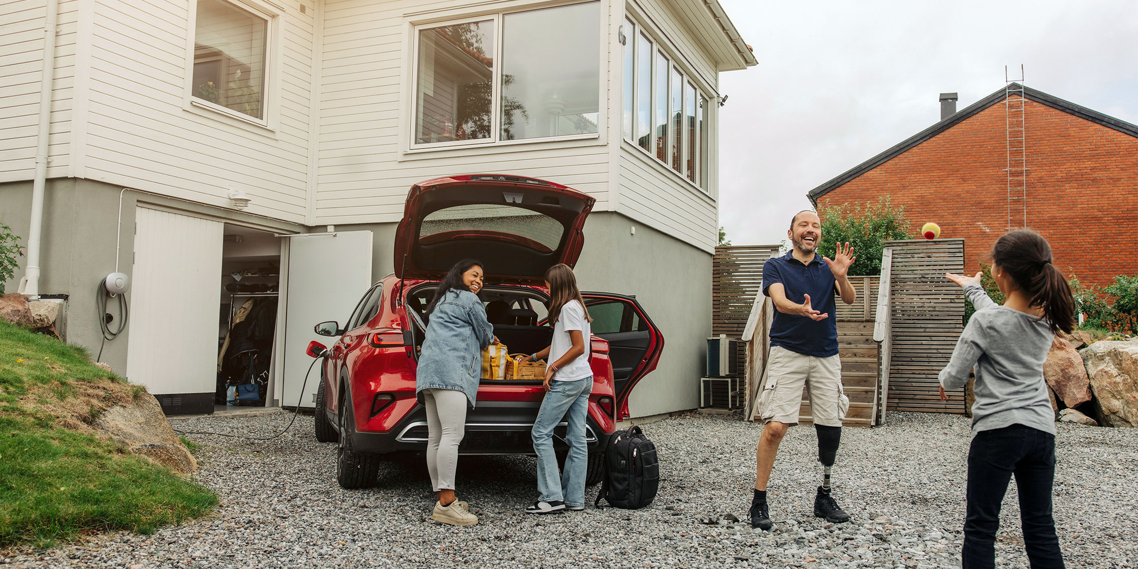 A photo of a family at home unloading groceries from the trunk of their car.