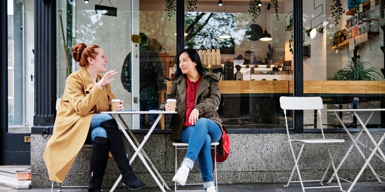Friends sitting outdoors and drinking coffee purchased with a Capital One rewards credit card.