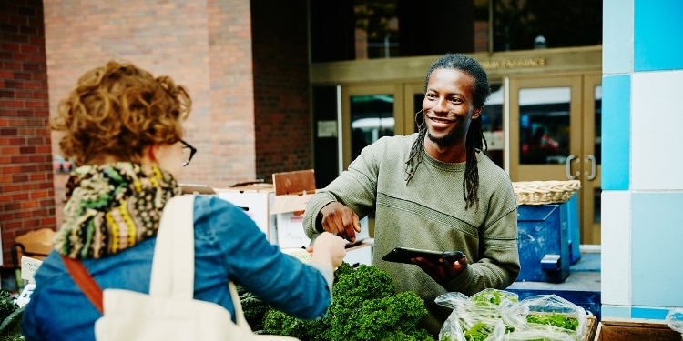 A smiling grocery store cashier accepting a credit card payment from a customer.