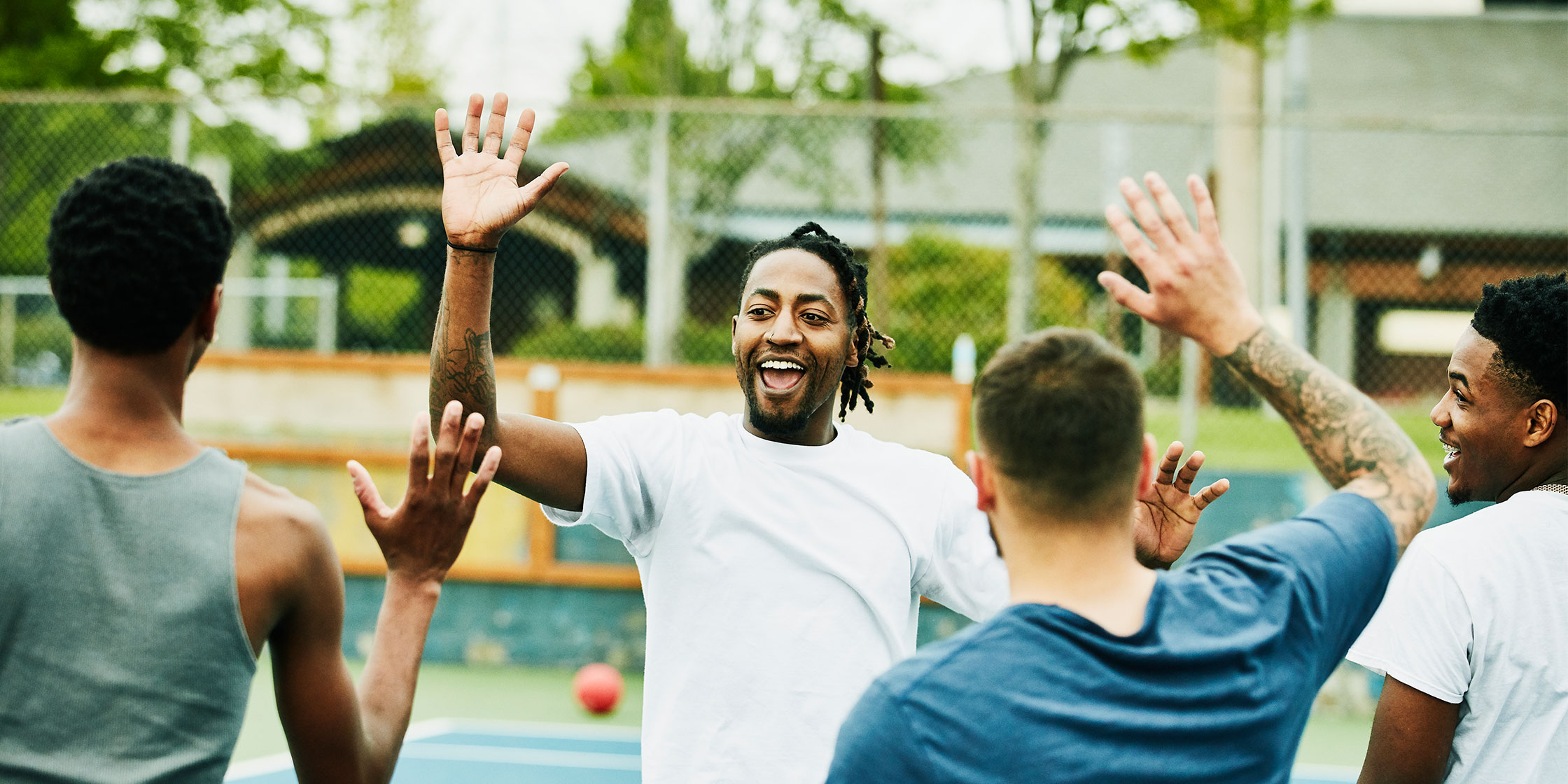 A group of diverse friends high-five each other while enjoying a game on an outdoor basketball court.