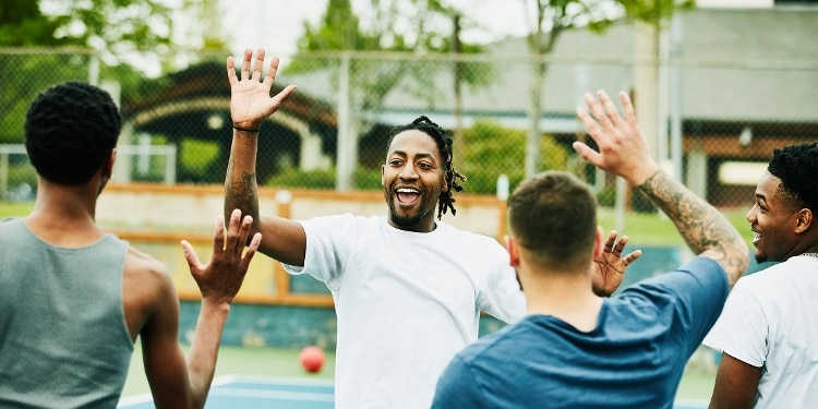 A group of diverse friends high-five each other while enjoying a game on an outdoor basketball court.