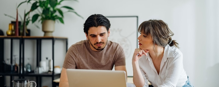 Two people looking at a laptop while considering a 401(k) hardship withdrawal.