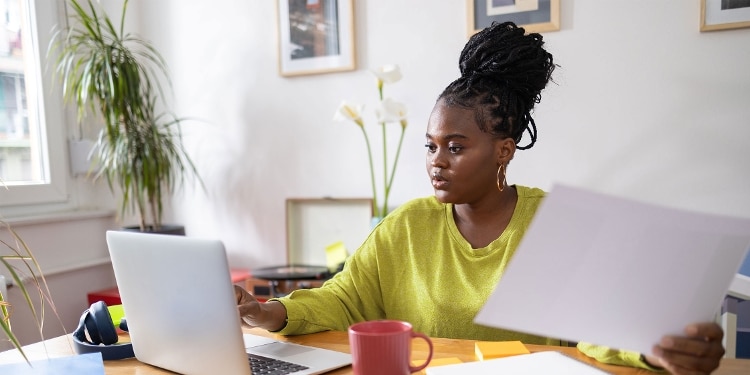 A woman types on her laptop while holding her credit card bill.