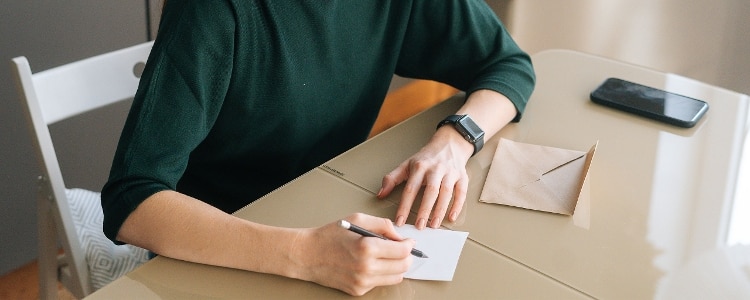 A person writing a note before addressing an envelope.