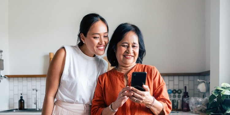 Mother and daughter checking their credit scores on a cellphone while standing in a kitchen.