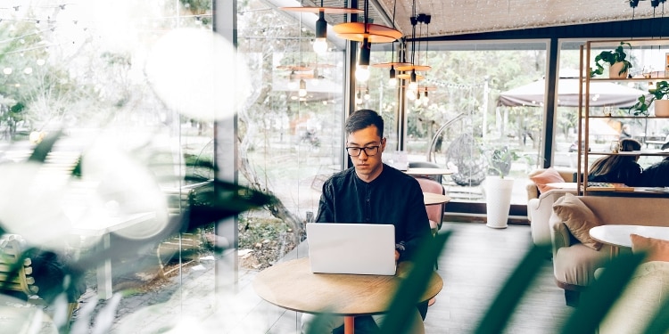 A person with bad credit sits in a coffee shop using a laptop to apply for a credit card.