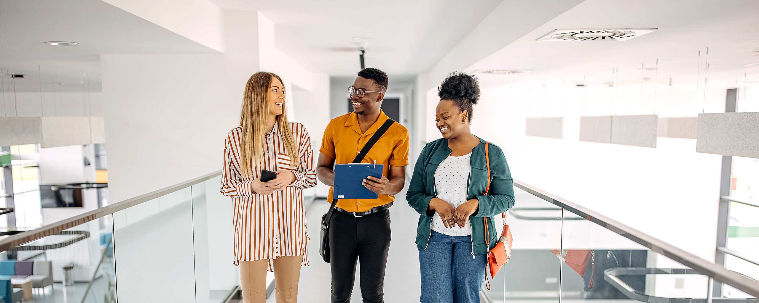 Three students standing in a walkway looking at each other and smiling.