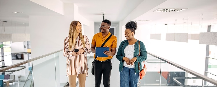Three students standing in a walkway looking at each other and smiling.