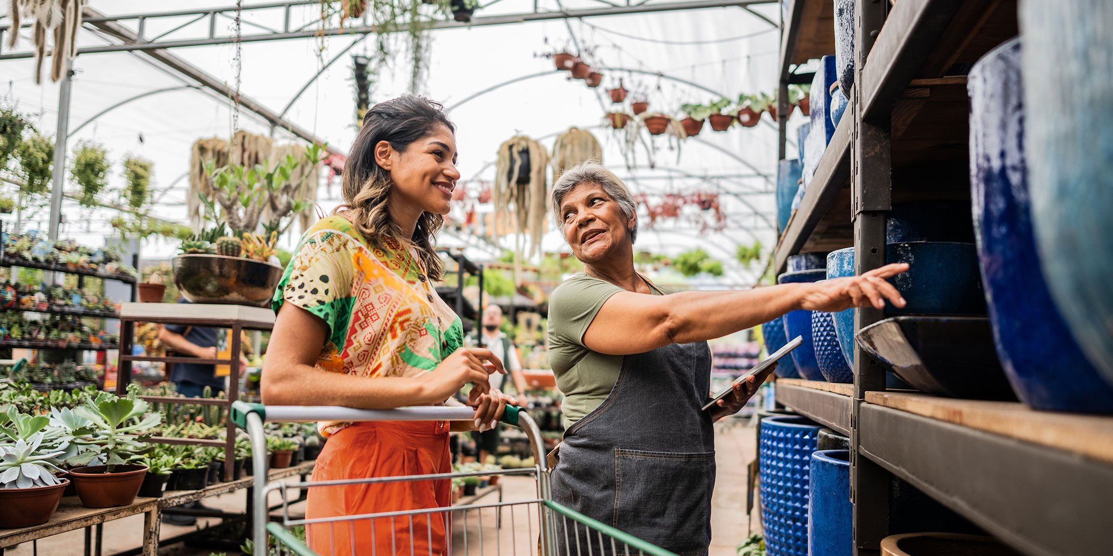 A person shops at a garden center and an employee helps them choose a ceramic pot.